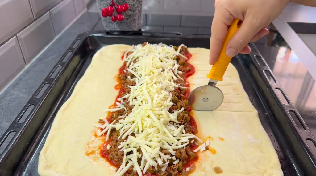 Unbaked closed pizza filled with minced meat and grated kashar cheese on baking tray