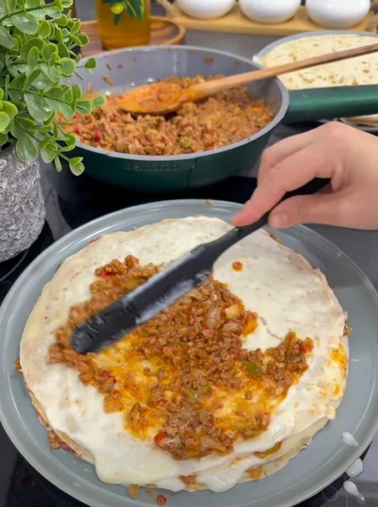Assembling Palace Layer with crepes, meat filling, and béchamel sauce in a baking dish