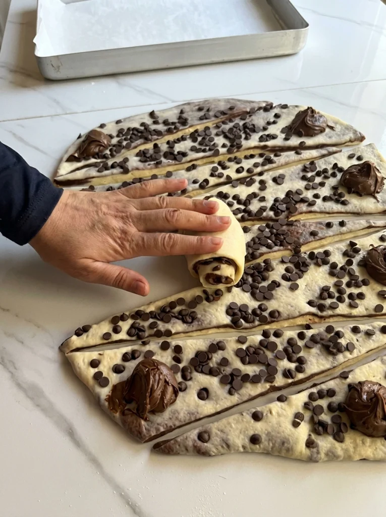 Unbaked chocolate croissant rolls brushed with egg yolk and topped with poppy seeds
