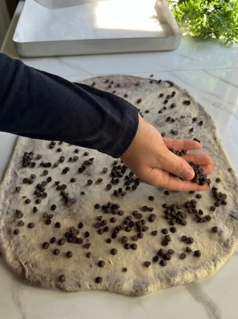 Hazelnut spread and chocolate chips being added to croissant dough triangles