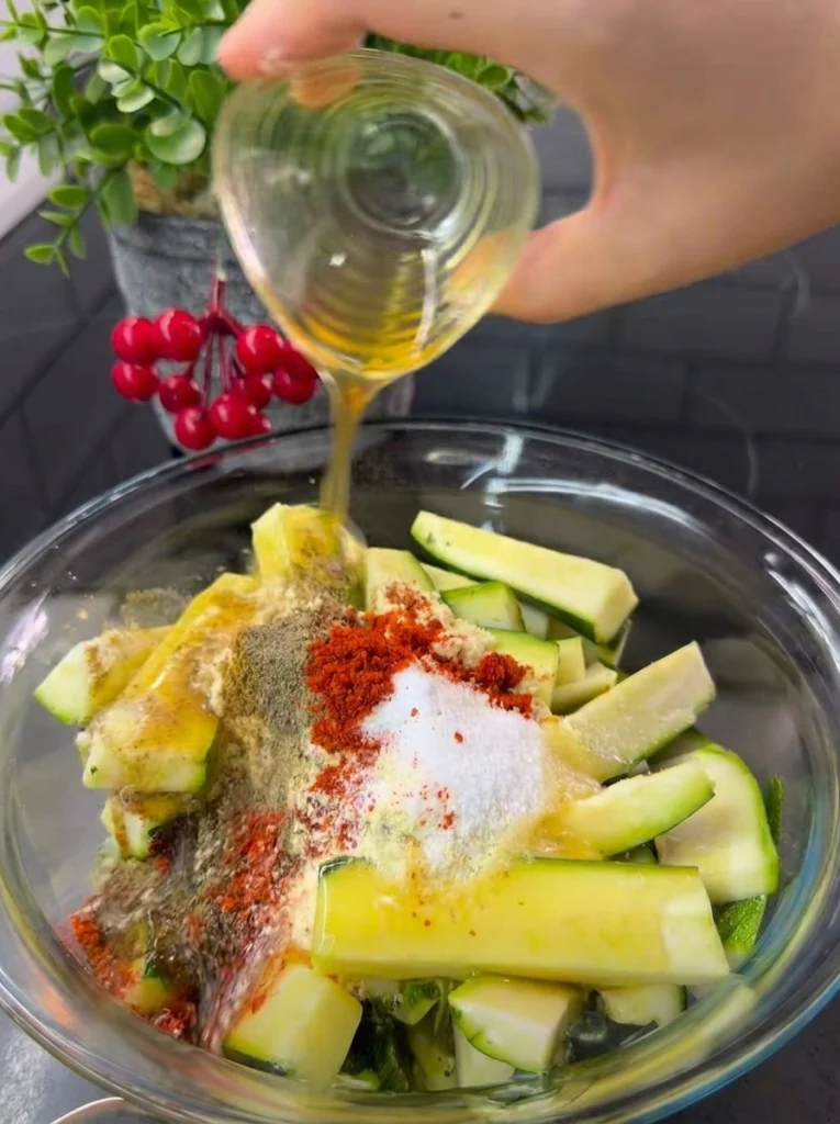 Raw zucchini slices being seasoned with spices and olive oil before baking