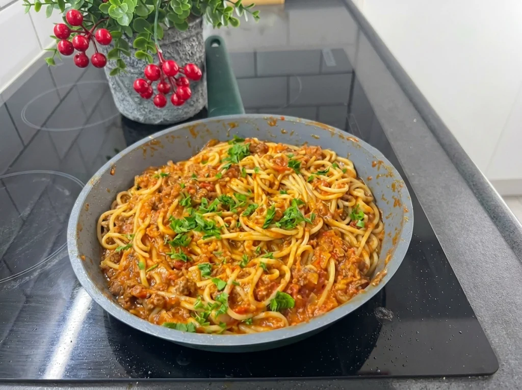 Spaghetti pasta with minced meat casserole topped with melted cheddar cheese and fresh parsley