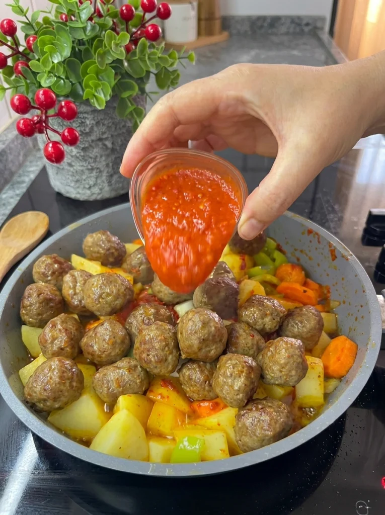 Tomato sauce and spices being stirred into vegetable stew