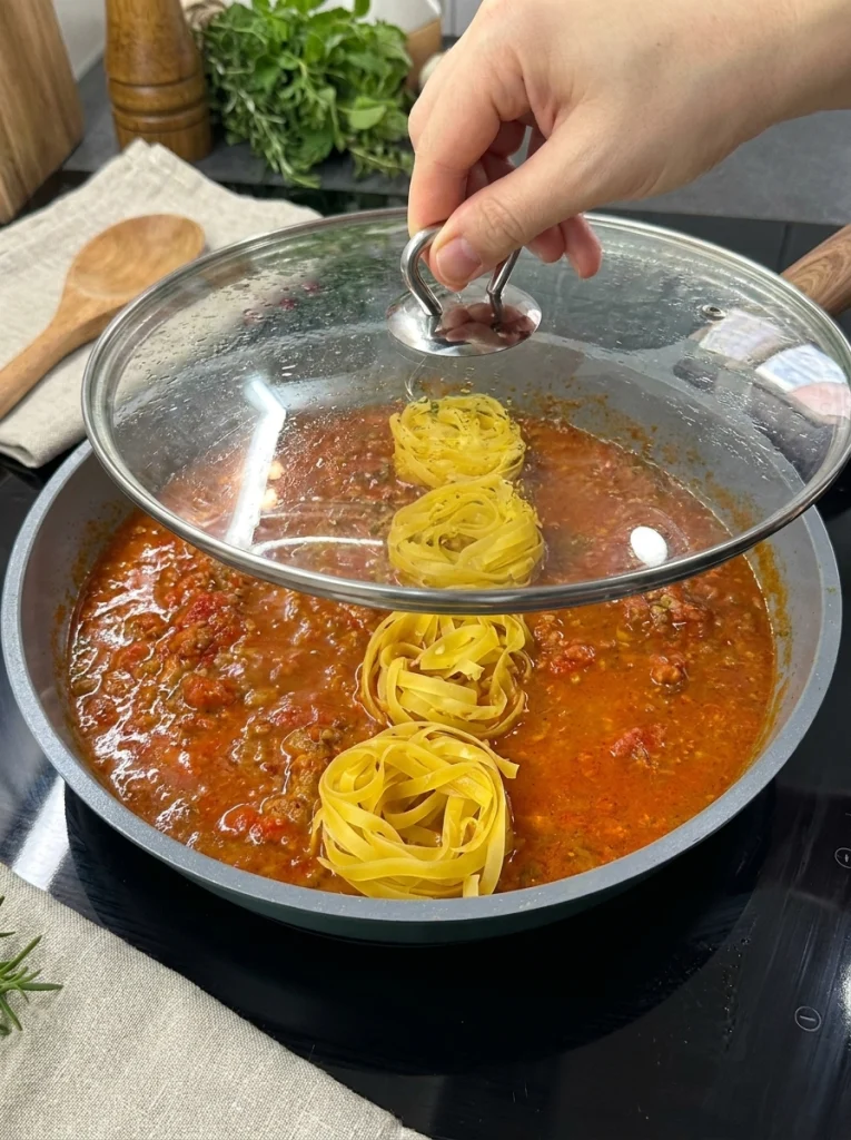 Uncooked pasta added to tomato vegetable sauce in a pan