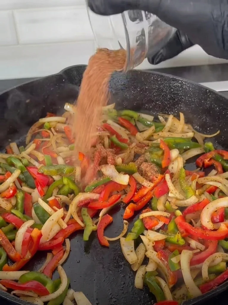 Charred bell peppers and onions cooking in a skillet for chicken fajitas