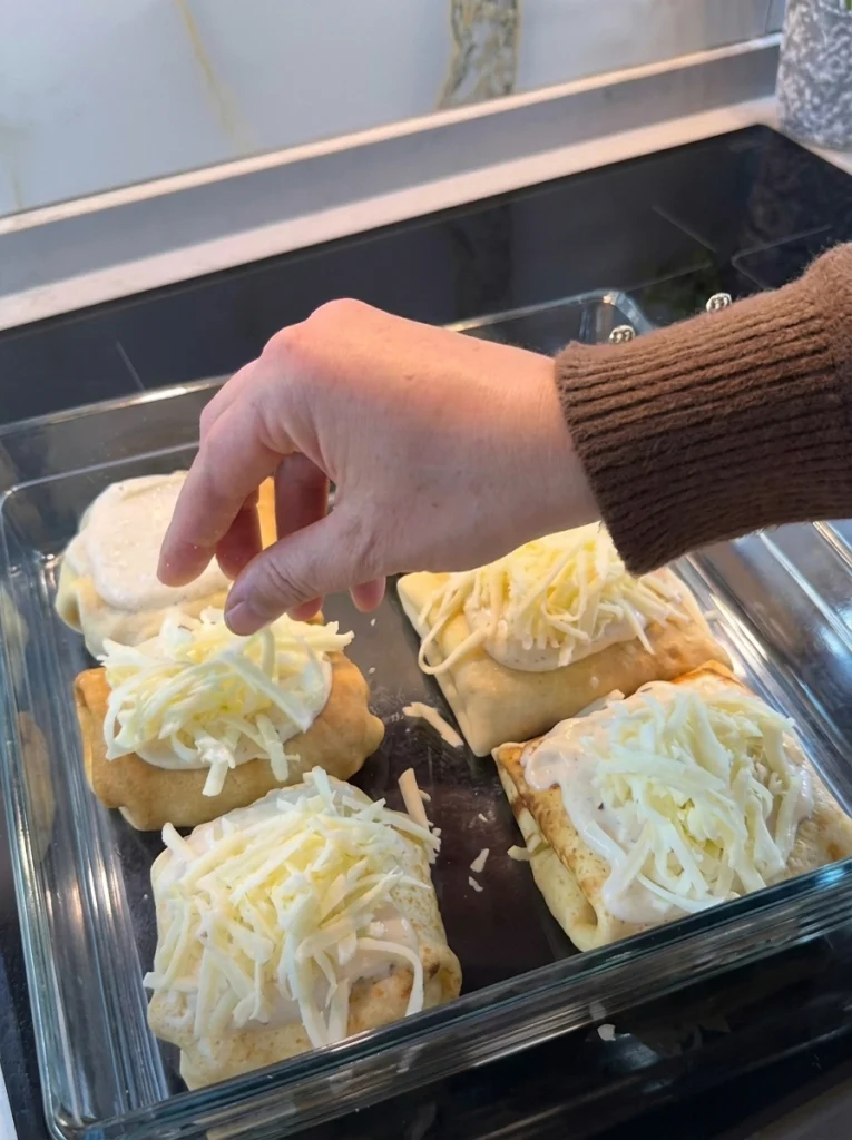 hicken crepe rolls arranged in a baking tray topped with béchamel and cheese