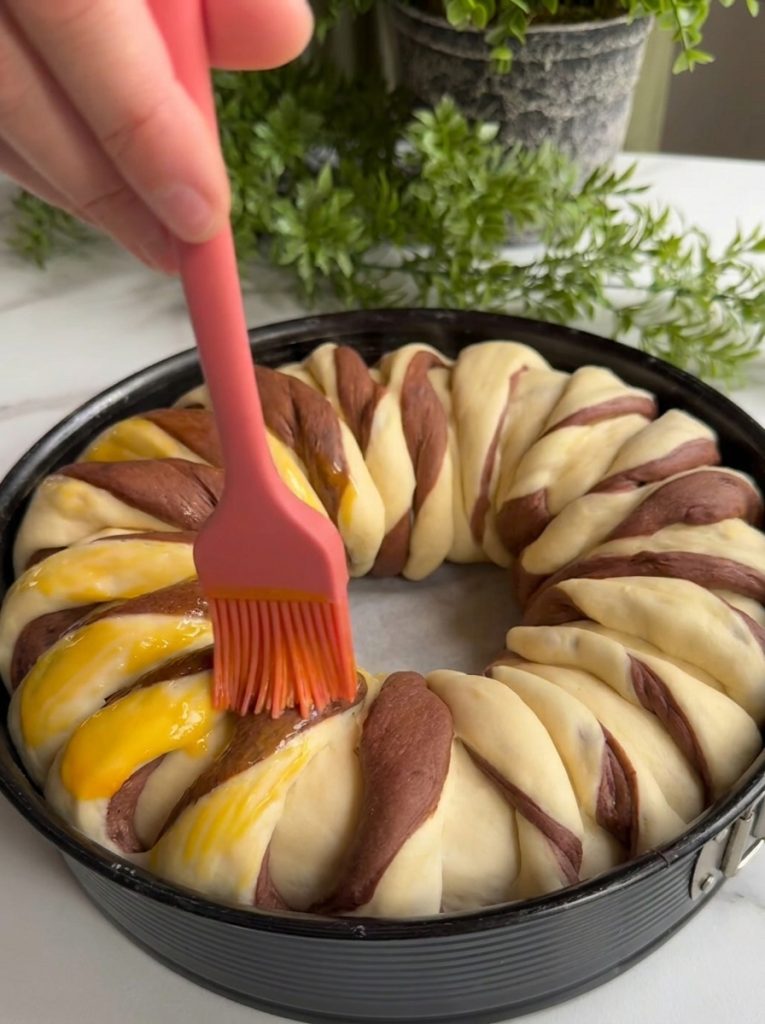 Brushing egg yolk on chocolate roll bread before baking