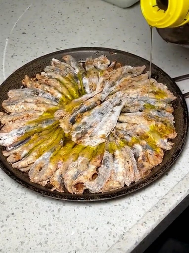 Anchovies frying golden in olive oil in a pan