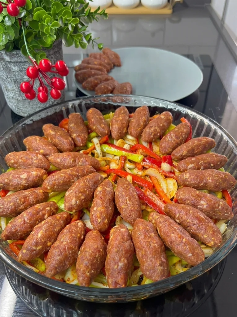 Uncooked meatballs arranged over sliced peppers and onions before baking